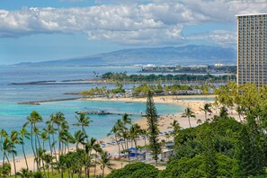 A beach with palm trees, a pier, and a tall building in the background.