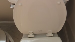 Et toilet med hvid skål og låg, håndsprit på tanken, og en beige væg.