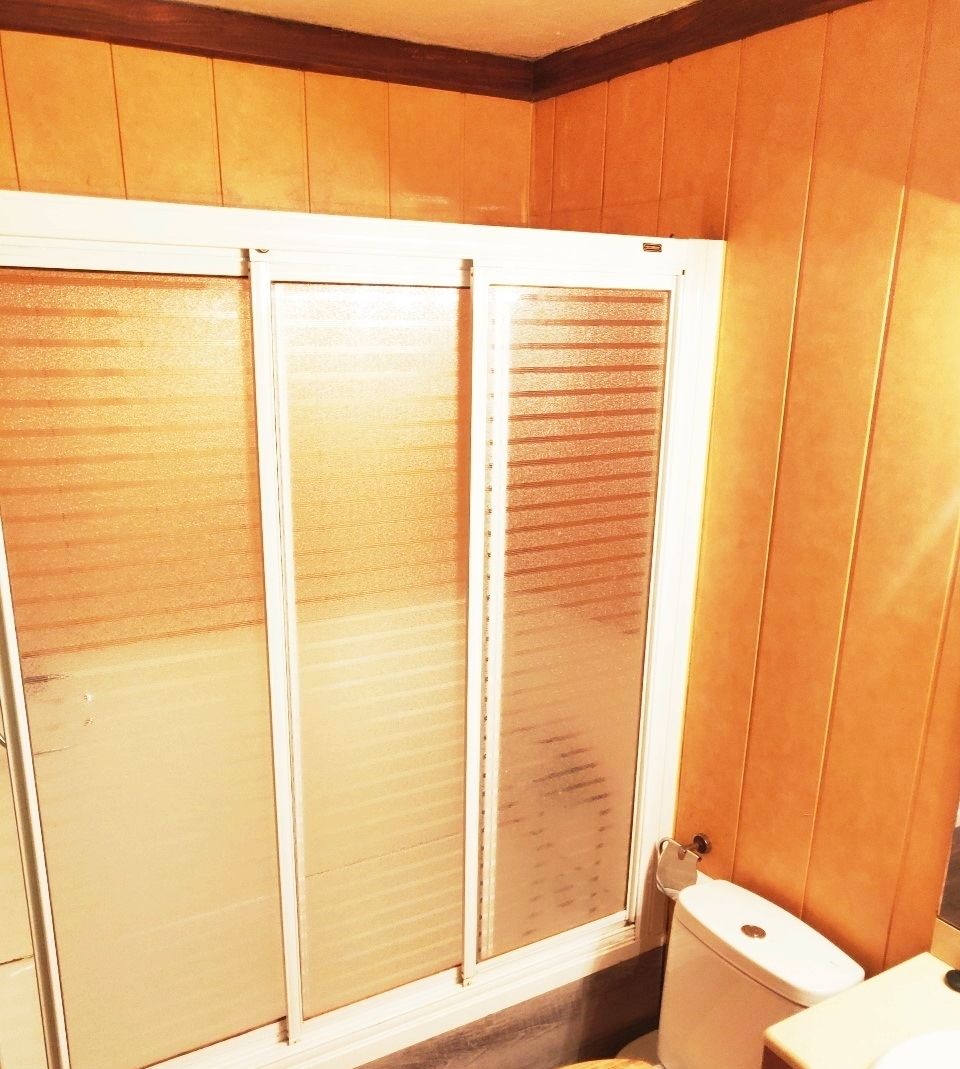 Casa de banho com painéis de madeira, sanita e chuveiro com portas de vidro jateado.