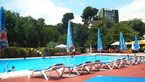 A swimming pool with lounge chairs and umbrellas, surrounded by greenery and a building in the background. - Beautiful Apartment, Swimming Pool and Beach 2 (Platja d'Aro)