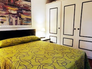 A hotel room with a bed, a nightstand, a lamp, and a wardrobe. - Beautiful Apartment, Swimming Pool and Beach 2 (Platja d'Aro)
