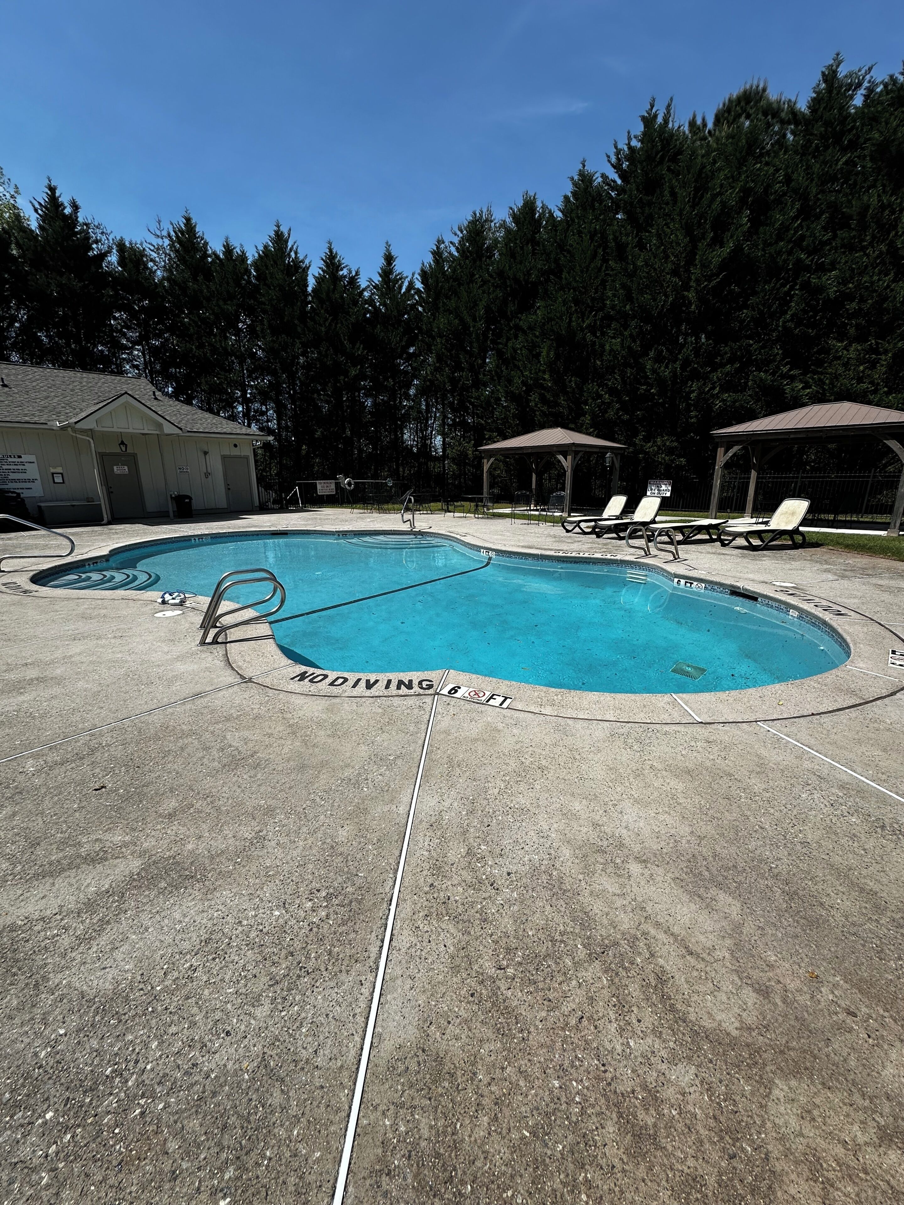 A swimming pool with a no diving sign, lounge chairs, and a gazebo.