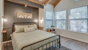 A bedroom with a bed, bedside tables, a ceiling fan, and large windows with blinds.