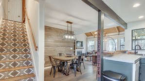 A modern kitchen with a central island, wooden staircase, and a dining area with a round table and chairs.