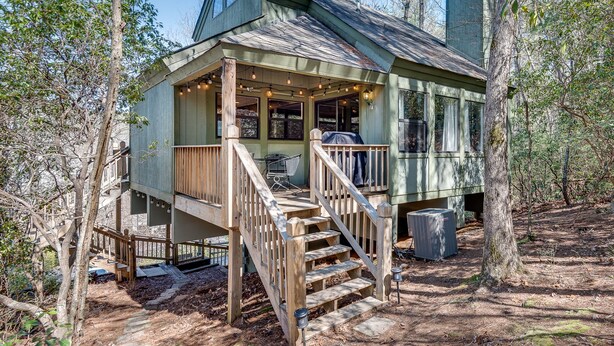 A wooden cabin with a porch, outdoor seating, and a staircase leading to the entrance.