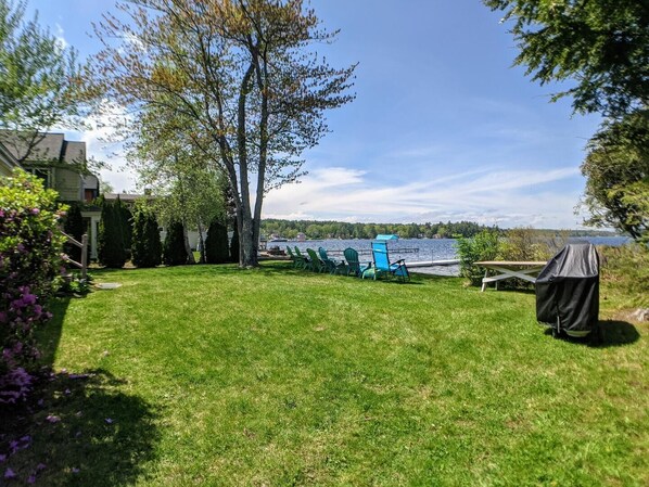 A backyard with a grassy lawn, a barbecue grill, and a view of a lake. - Endless Summer Cottage (Gilford)