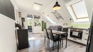 A modern kitchen with a dining area, featuring a skylight, a black pendant light, and a view of the outdoors.