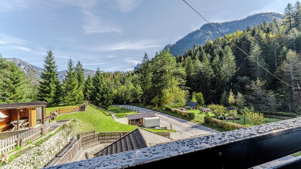 A mountain lodge with a wooden cabin, a covered outdoor seating area, and a view of a forested mountain range.