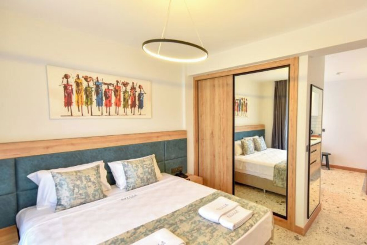 A hotel room with a bed, a mirror, a wooden headboard, and a painting on the wall.