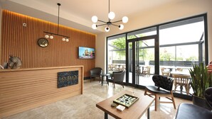 A modern reception area with a wooden panel wall, a clock, a television, and a large window offering a view of the outdoors. - Avilia Suites (Fethiye)