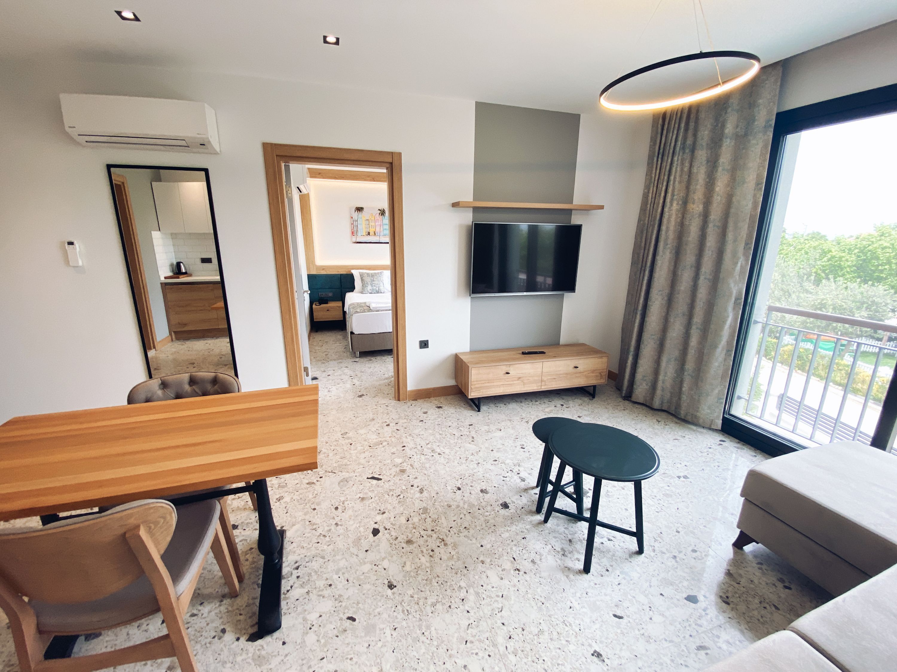 Una moderna camera d'albergo con angolo cottura, una TV a parete, un divano, un tavolo da pranzo con sedie e un balcone con vista.