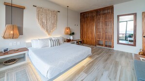 A spacious bedroom with a large bed, wooden headboard, and a view of the sea through a window. - Eco-Friendly Oceanfront Penthouse W/ Beach Access (Huatulco)