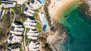 An aerial view of a coastal resort with multiple buildings, a beach, and clear turquoise water. - Eco-Friendly Oceanfront Penthouse W/ Beach Access (Huatulco)