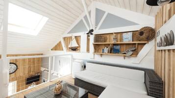 A cozy interior with a loft-style ceiling, a sofa, a coffee table, and a bookshelf with various items.