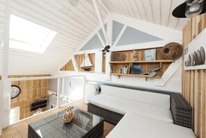 Een gezellig interieur met een loft-stijl plafond, een bank, een salontafel en een boekenplank met diverse spullen.