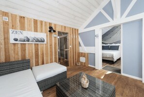 Een kamer met een bed, een bank, een tafel met een decoratief object, houten lambrisering, een deur naar een balkon en een wandlamp.