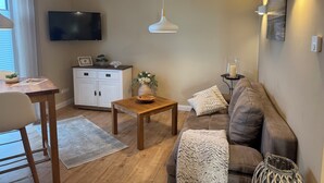 Een woonkamer met een houten tafel, een bank en een aan de muur bevestigde televisie.