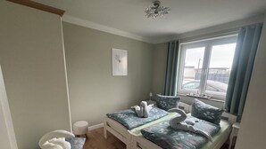 Een slaapkamer met een bed, een klein rond krukje, een zacht vloerkleed, een raam met gordijnen en een plafondlamp.