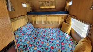 A compact RV interior with a bed, a window, and a small table. - Vintage Trailer with  access to Big Lake & Private Campground  (Big Lake)