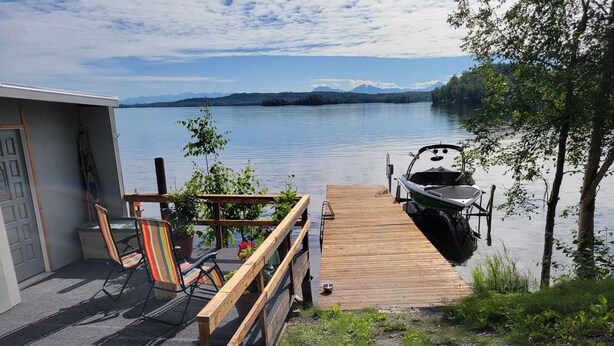 A wooden dock extending into a calm lake with a boat docked on the right. A small building with a door and windows is visible on the left. - Vintage Trailer with  access to Big Lake & Private Campground  (Big Lake)