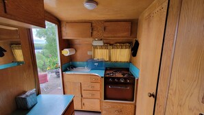A compact kitchen with wooden cabinets, a sink, a stove, and a window overlooking greenery. - Vintage Trailer with  access to Big Lake & Private Campground  (Big Lake)