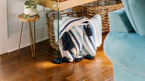 Een houten console tafel met daarboven een schilderij van een strand, een potplant en een geweven mand.