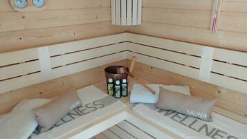 A sauna room with two benches, towels, bottles of essential oils, and a wooden heater.