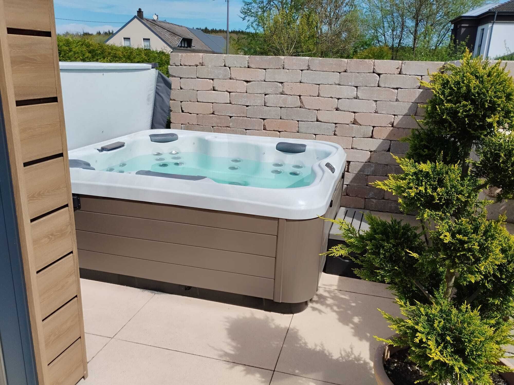 A hot tub in an outdoor setting with a brick wall and a small tree nearby.