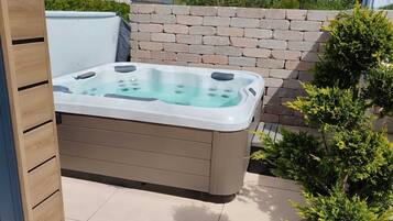 A hot tub in an outdoor setting with a brick wall and a small tree nearby.