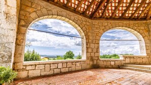 Habitación con paredes de piedra y dos grandes ventanales en arco que dan a vistas de vegetación y colinas lejanas.