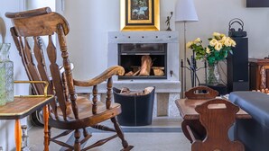Una sala de estar con chimenea, un televisor montado en la pared y un sillón mecedor de madera.