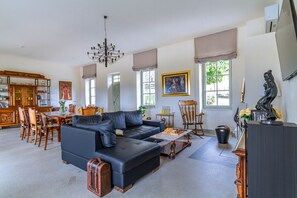 Un salón amplio con un sofá de cuero oscuro, una mesa de comedor de madera y una araña.