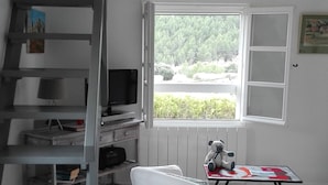 Ein Zimmer mit Treppe, einem weißen Sofa, einem Tisch mit einem Fischgemälde und einem Fenster mit Blick auf Grünflächen.