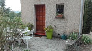 Ein Haus mit roter Tür, einem kleinen Fenster mit Schild „Willkommen“ und einem grünen Blumenkasten mit Blumen.