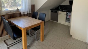 Une cuisine moderne avec un coin repas, comprenant une table et des chaises en bois, une fenêtre avec des rideaux et une vue sur la verdure à l’extérieur.