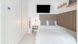 A bedroom with a bed, a TV mounted on the wall, a bedside table with a lamp, and a striped headboard. - Minimalist Studio 3 Minutes Walk to Las Canteras Beach (Las Palmas de Gran Canaria)