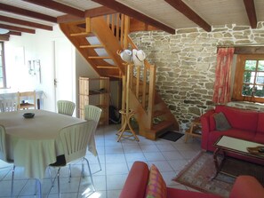 Un vaste espace de vie agrémenté d’un escalier en bois, d’un mur en pierre, d’un canapé rouge et d’une table à manger avec des chaises.