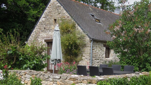 A stone building with a sloped roof, a small window, and a patio area with outdoor furniture.