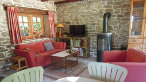 A cozy living room with a stone wall, a red sofa, a television, a bookshelf, and a fireplace.