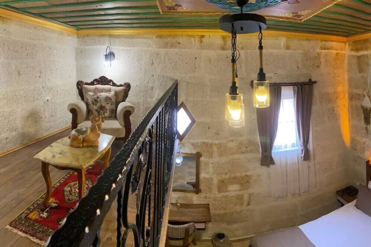 Una habitación con pared de piedra rústica, escalera de madera, una mesa de comedor con sillas y cama con cabecera.