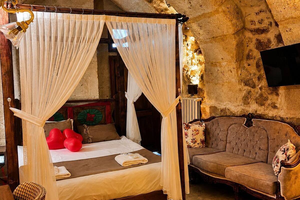 Una cama con dosel, un sofá, un televisor de pantalla plana y un tapete decorativo en una habitación con paredes de piedra.