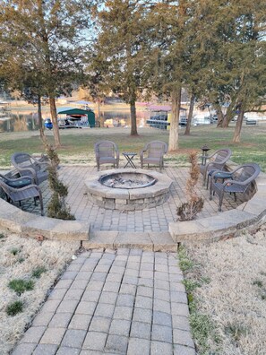 Un foyer entouré de fauteuils en osier et d’une petite table, avec un chemin pavé menant à un lac.