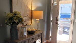 A hallway with a wooden console table, a vase of flowers, a lamp, and a framed artwork on the wall.