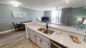 A modern kitchen with a large island, stainless steel sink, and a dining area with a table and chairs.