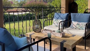 An outdoor patio with a wooden table, two cushioned benches, and a metal railing.