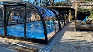 A covered swimming pool with a pergola and lounge chairs.