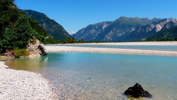 A clear lake with a rocky shore and mountains in the background.