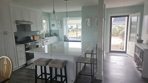 A modern kitchen with a large island, bar stools, and a view of the backyard. - Ocean & Wetland views, 3 decks, steps from the beach, 4 BRs, sleeps 10. (Oak Island)