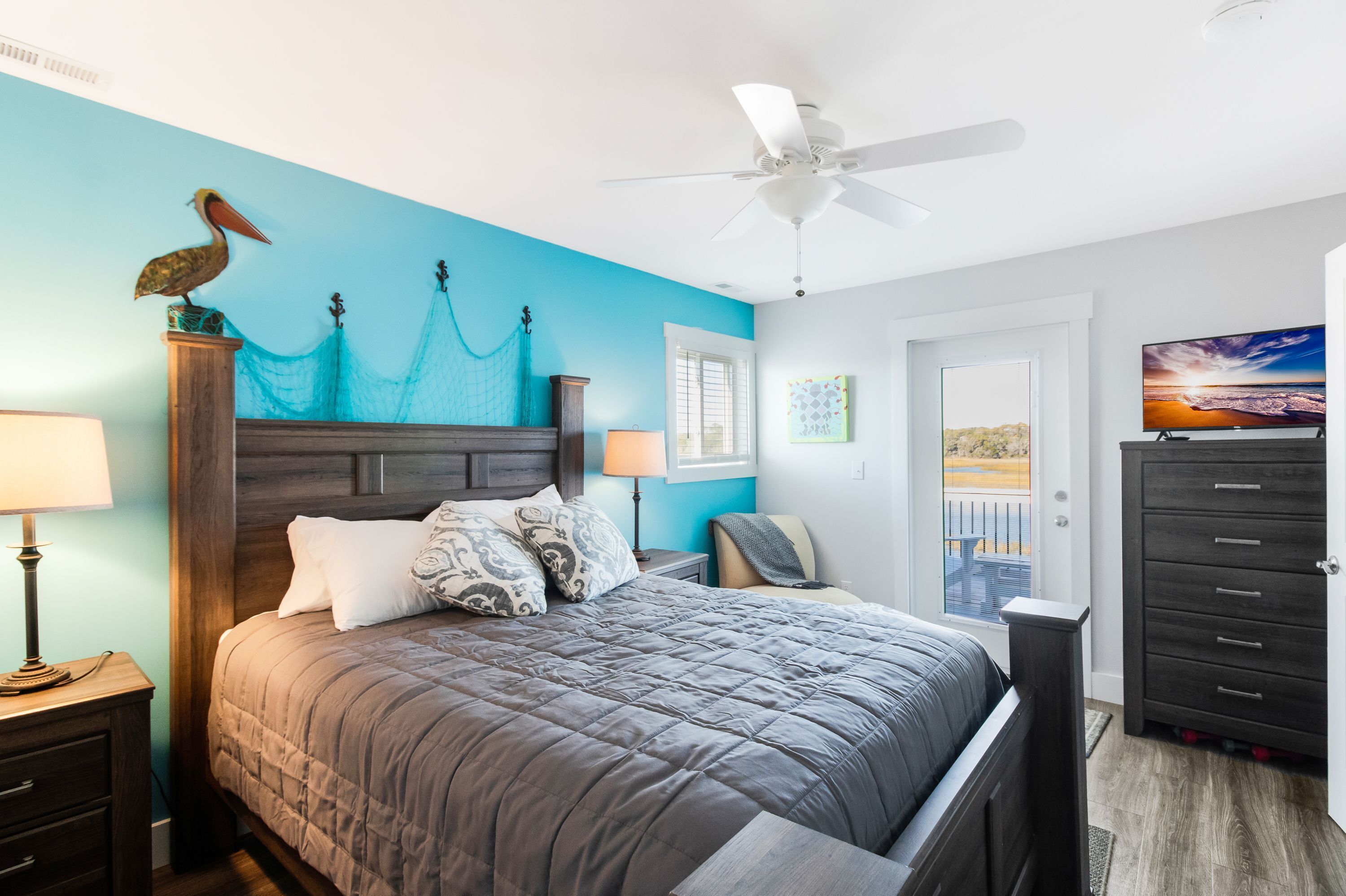 Une chambre à coucher comprenant un lit, un ventilateur de plafond, une table de chevet en bois, une commode et un téléviseur.