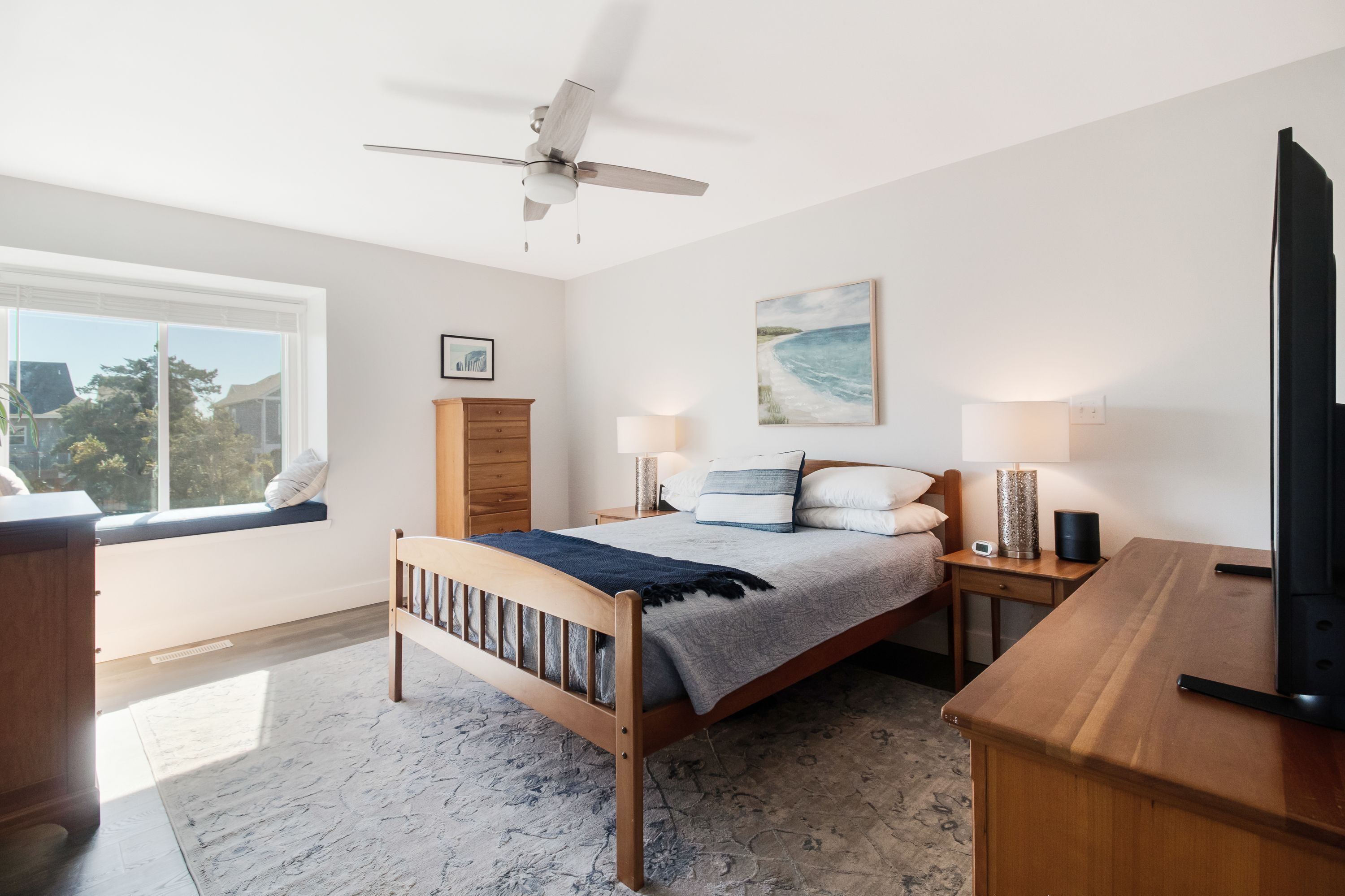 A bedroom with a wooden bed, a nightstand with a lamp, a TV, and a window with a view of trees.